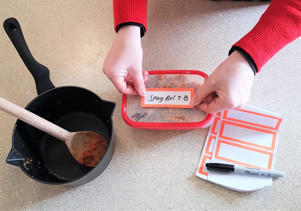 Hands placing a label on a container of left over spaghetti bol