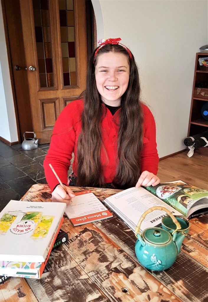 Young woman smiling at the camera while filling out a weekly meal menu plan