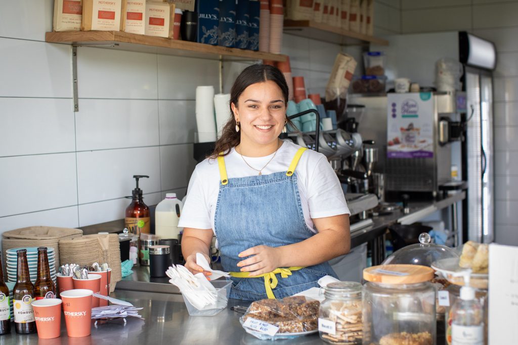 A staff member smiling as she stands behind the counter at Hub Cafe Woolgoolga