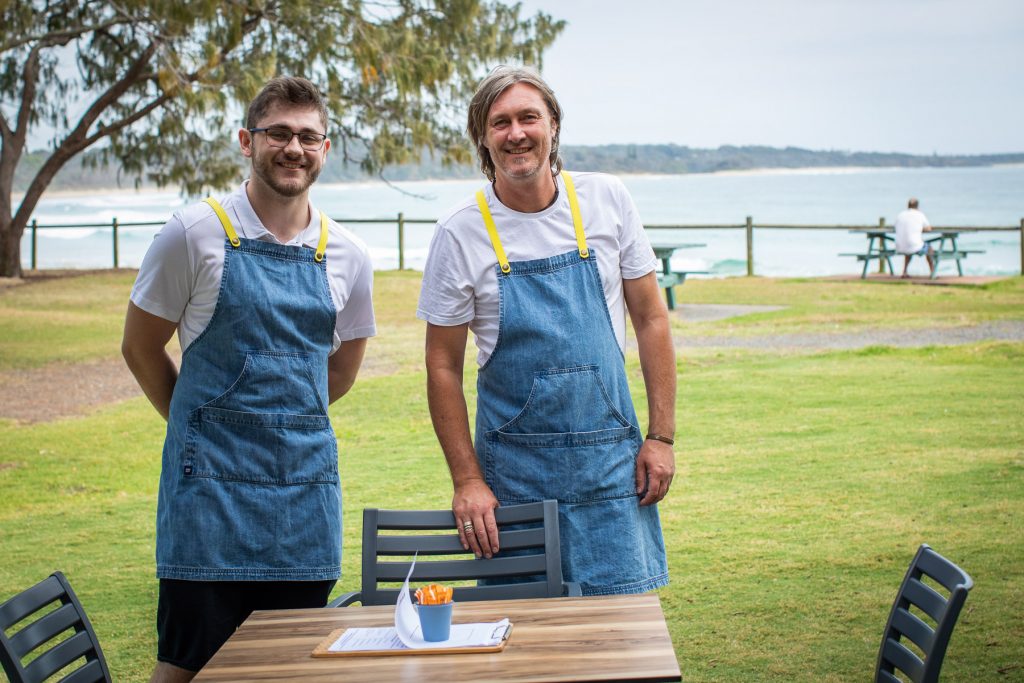 Two staff members at Hub Cafe with Woolgoolga's main beach in the background 2