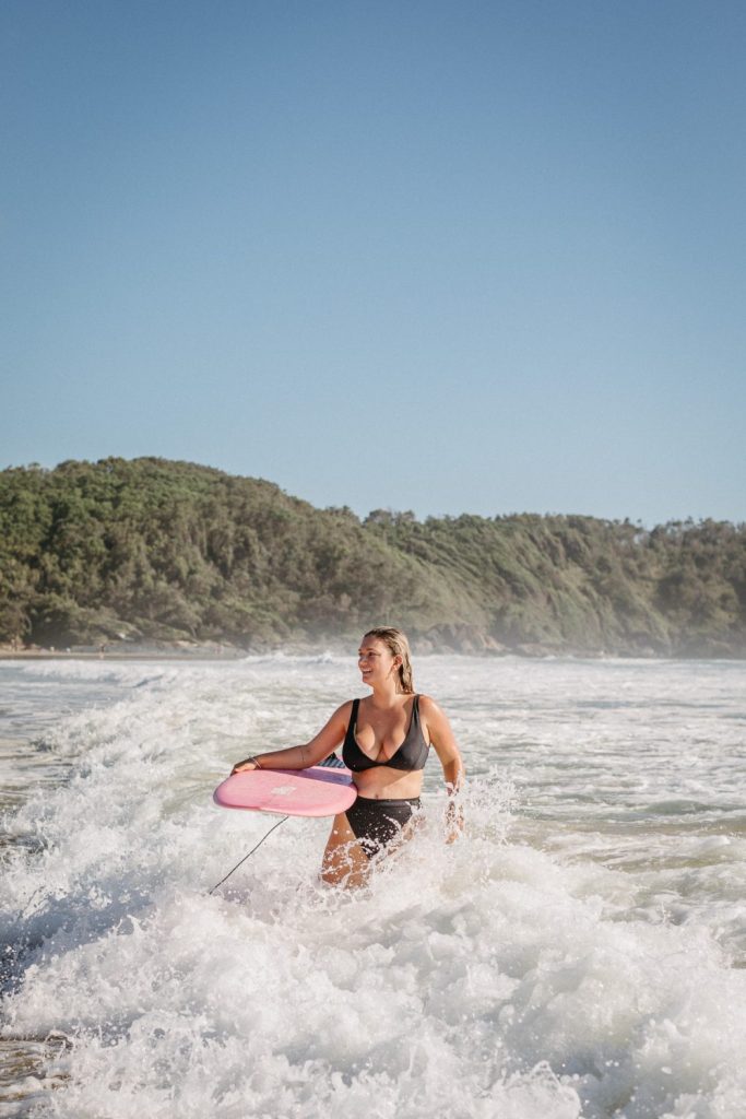 Woman standing in the ocean holding a pink surfboard 