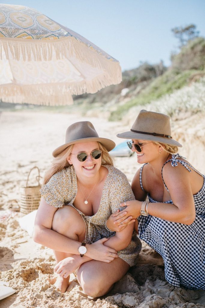 Mid shot of two women wearing Akubra hats on the beach