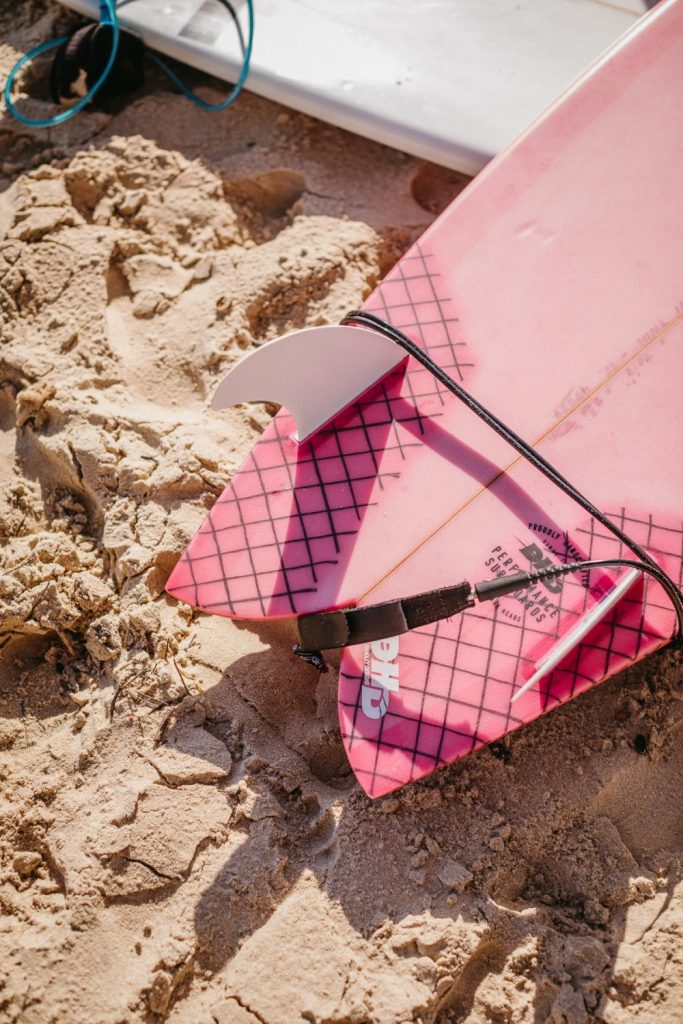 The tail and fins of a pink DHD surf board on the sand