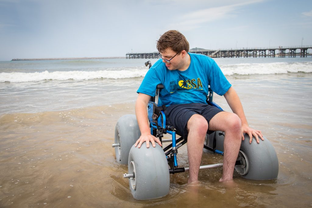 Mid shot of Brendan Harvey using a beach wheelchair in the water at Jetty Beach