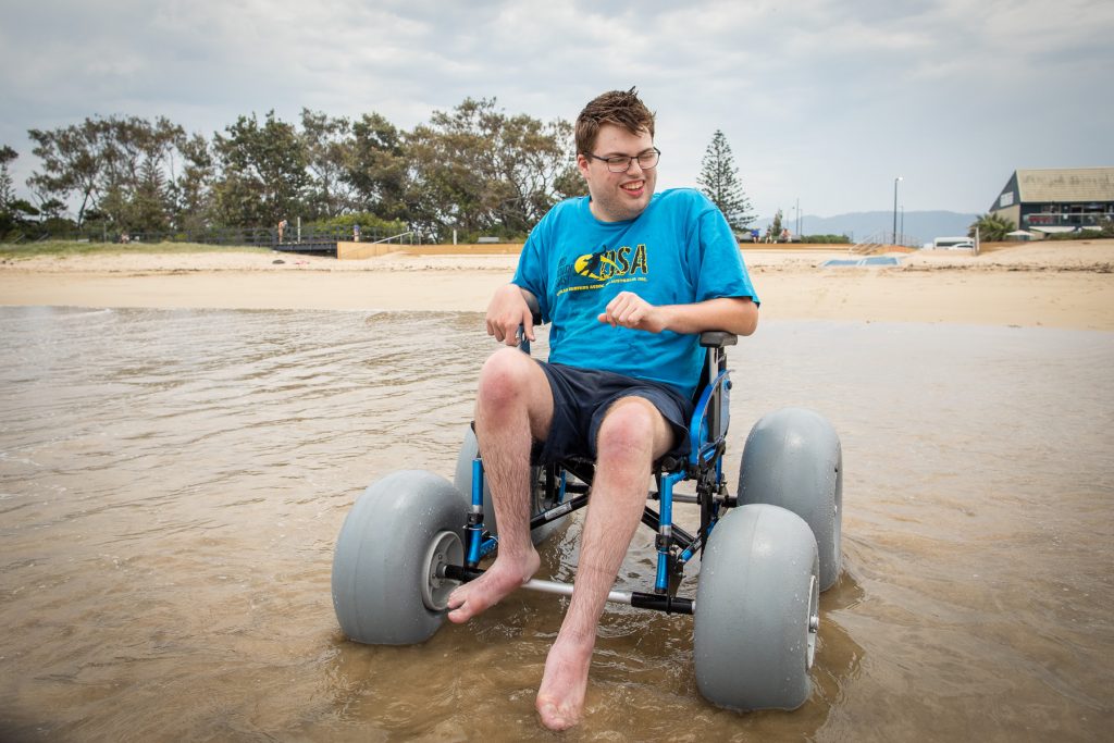 Mid shot of Brendan Harvey using a beach wheelchair in the water at Jetty Beach