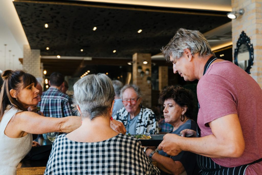 People sitting at a table accepting food from a chef