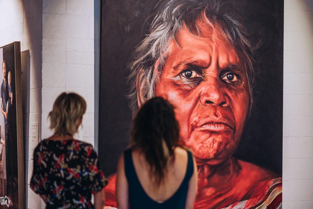 Two women looking at a large portrait in a gallery 