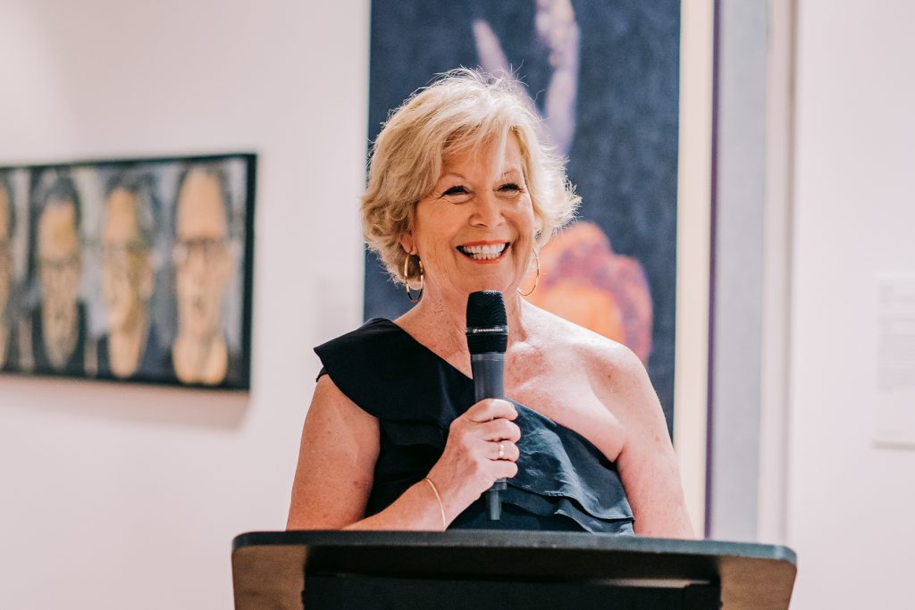 A smiling woman holds a microphone and gives a speech