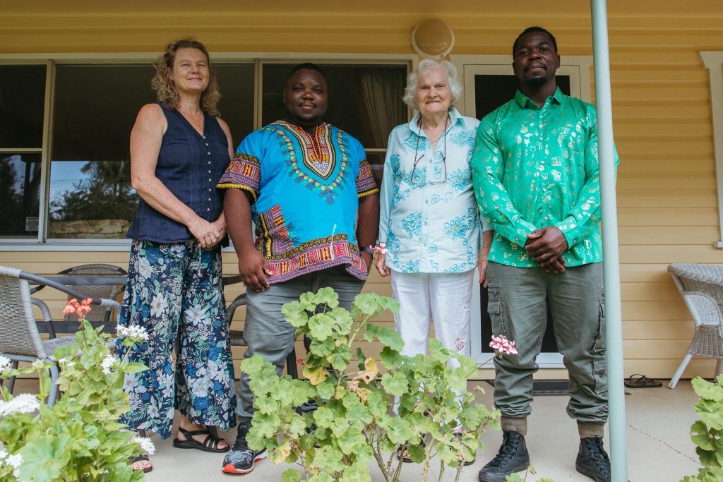 Mid shot of four smiling people standing next to plants. 