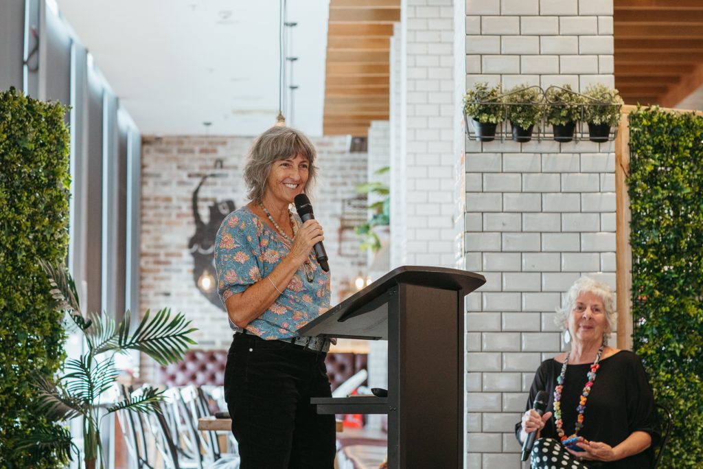 Mid shot of a smiling woman speaking into a microphone at a lectern