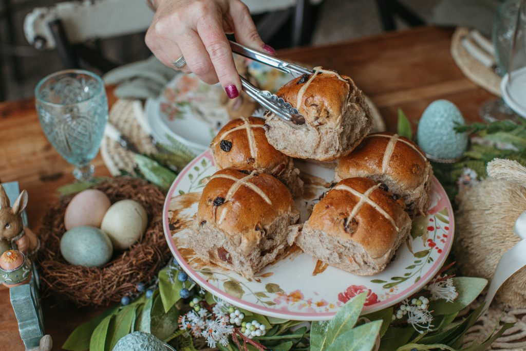 A hand holding tongs and placing a hot cross bun onto a tray