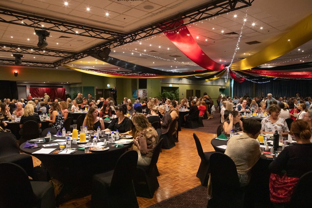 Wide shot of many women sitting at tables eating breakfast