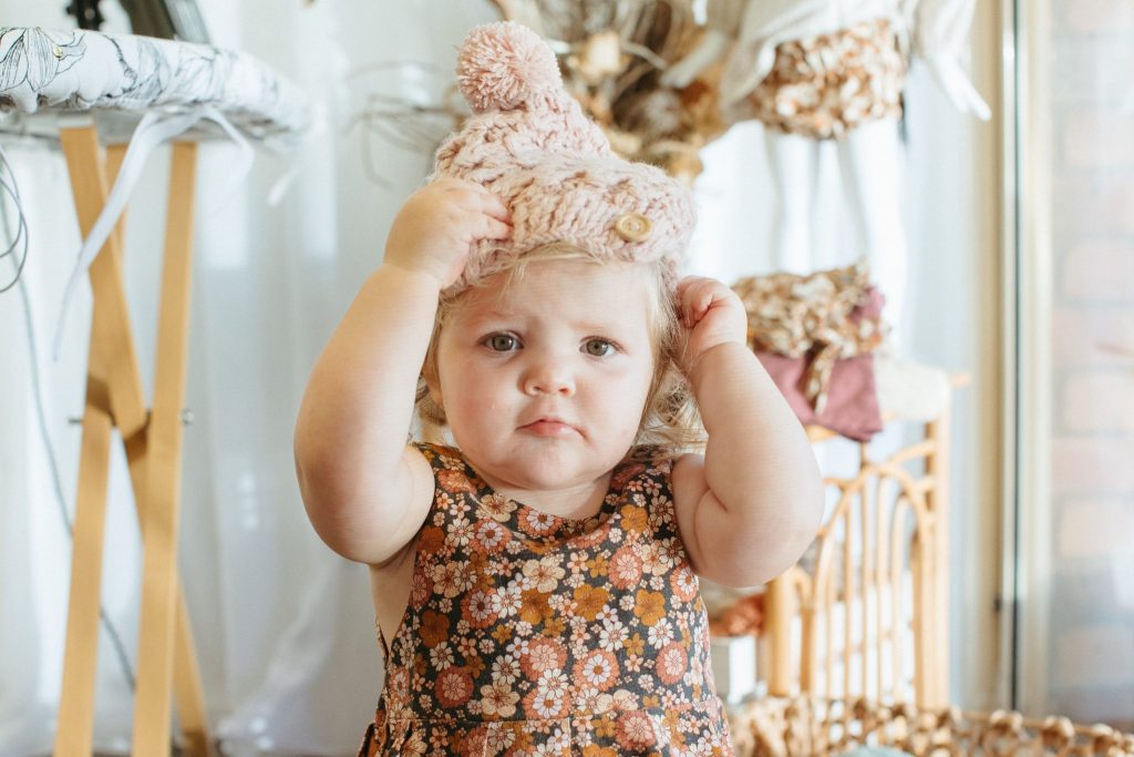 A toddler pulls a pink beanie onto her head