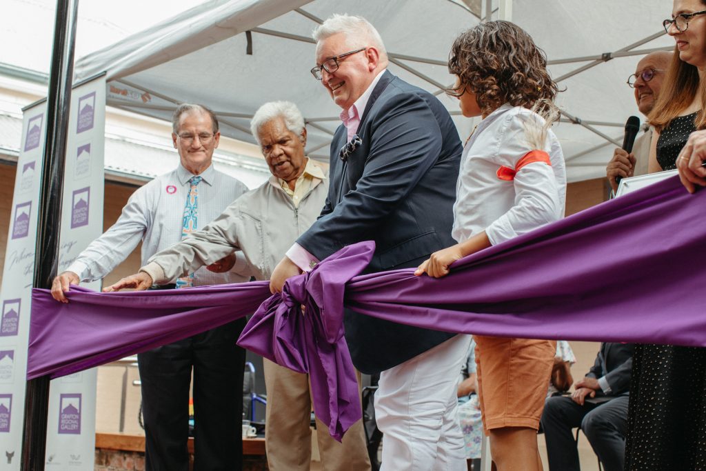 Three men and a boy cutting a large purple ribbon