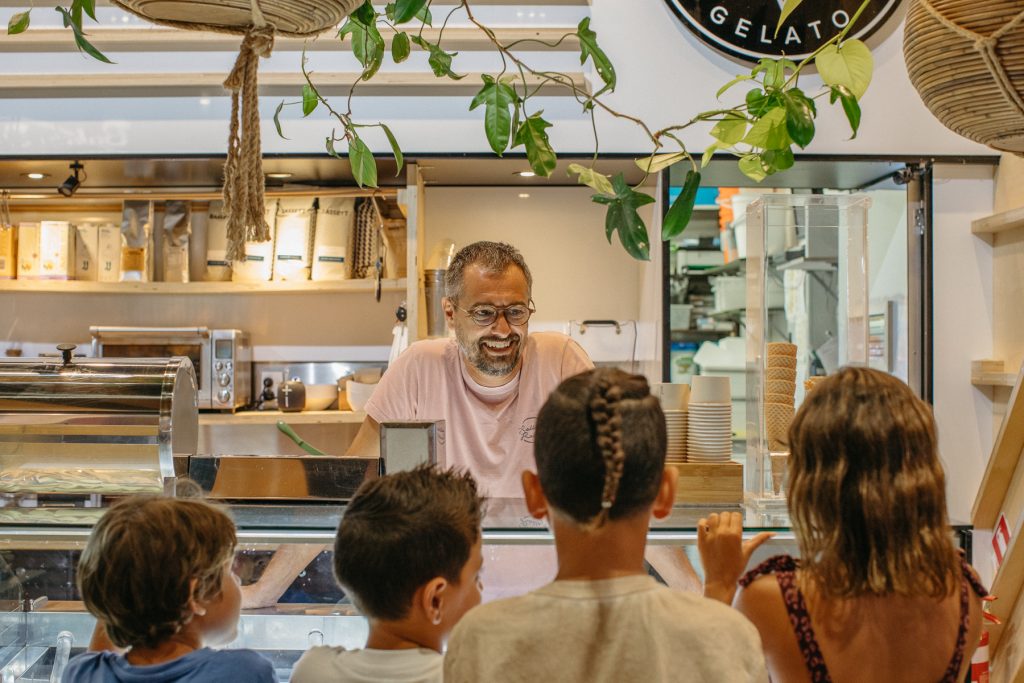 A smiling man peering over a cabinet full of gelato