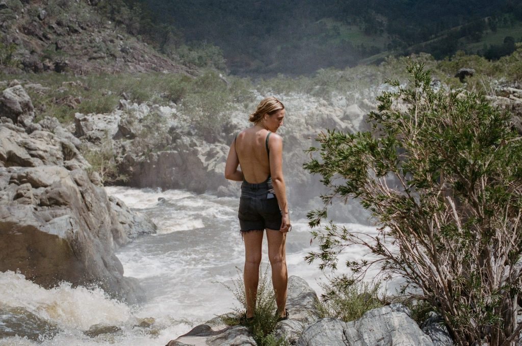 A woman standing on rocks above a rushing river