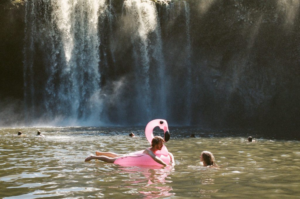 Wide shot of a couple swimming below a waterfall 