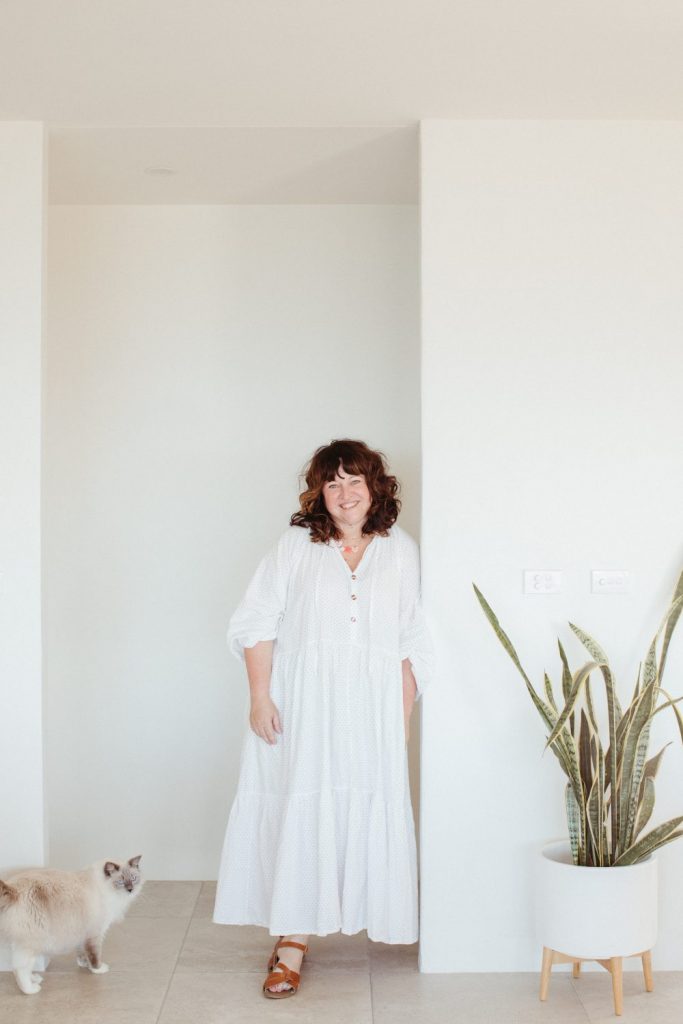 A smiling woman leaning against a white wall