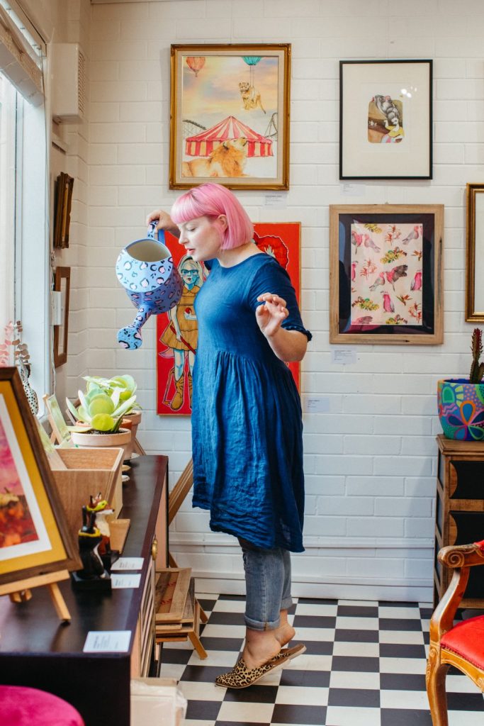 A woman with pink hair pretending to pour water on plants