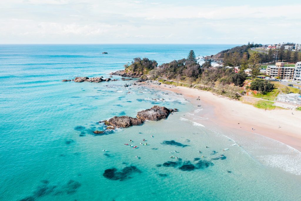 Drone shot of surfers in the ocean beside a rock formation