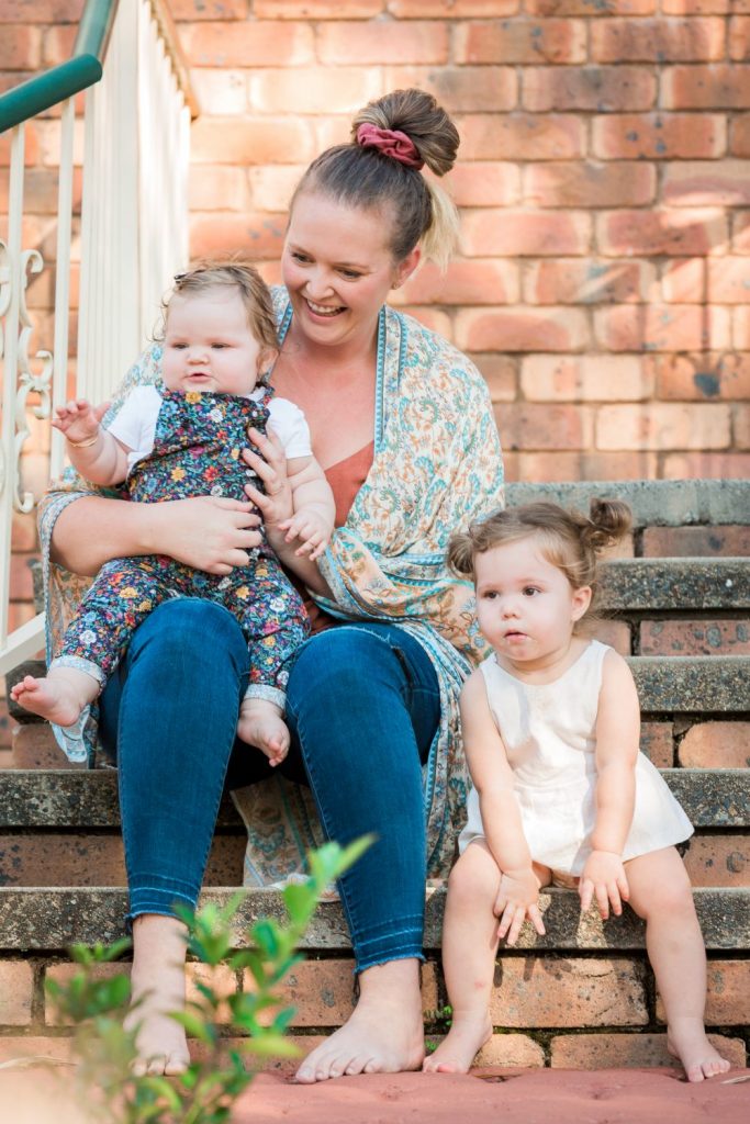 A woman holds baby with a toddler sitting next to her 