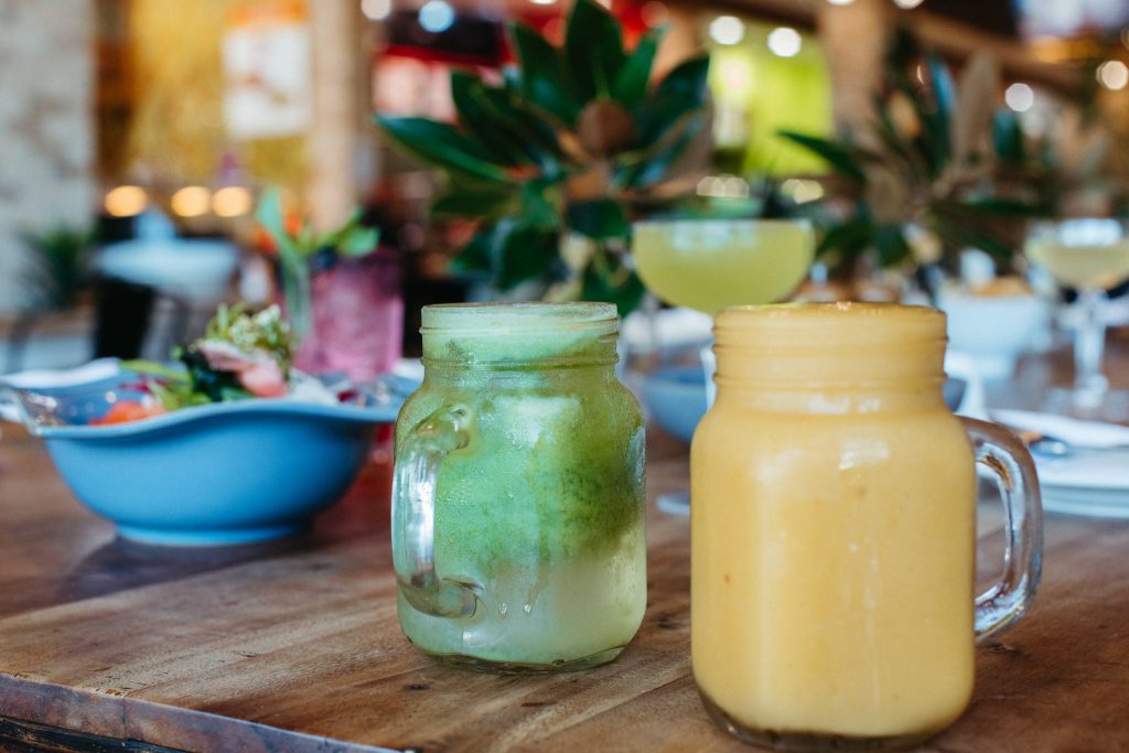 Close up of a green juice and a mango smoothie in glass jars on a wooden table 
