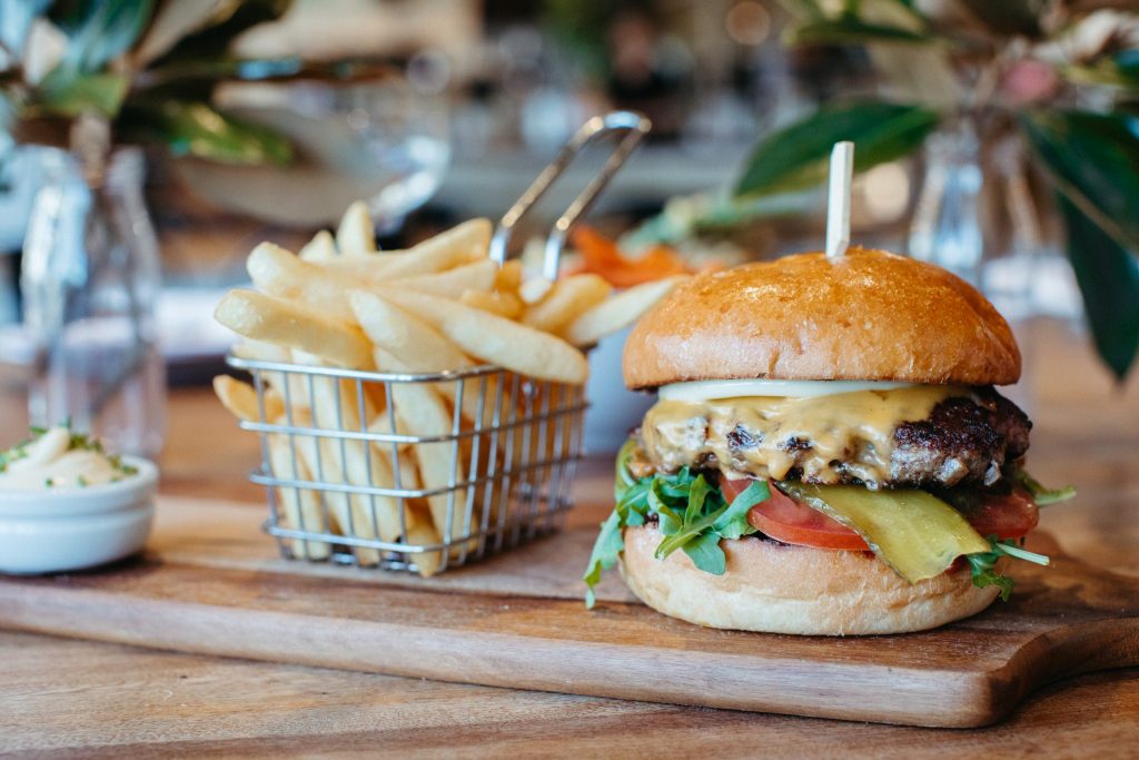 Close up of a beef burger and fries on a wooded chopping board 