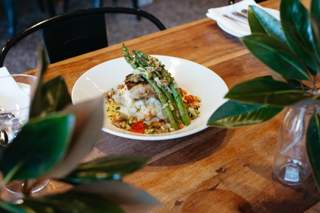 Mid shot of baked fish and asparagus in a white bowl on a wooden table