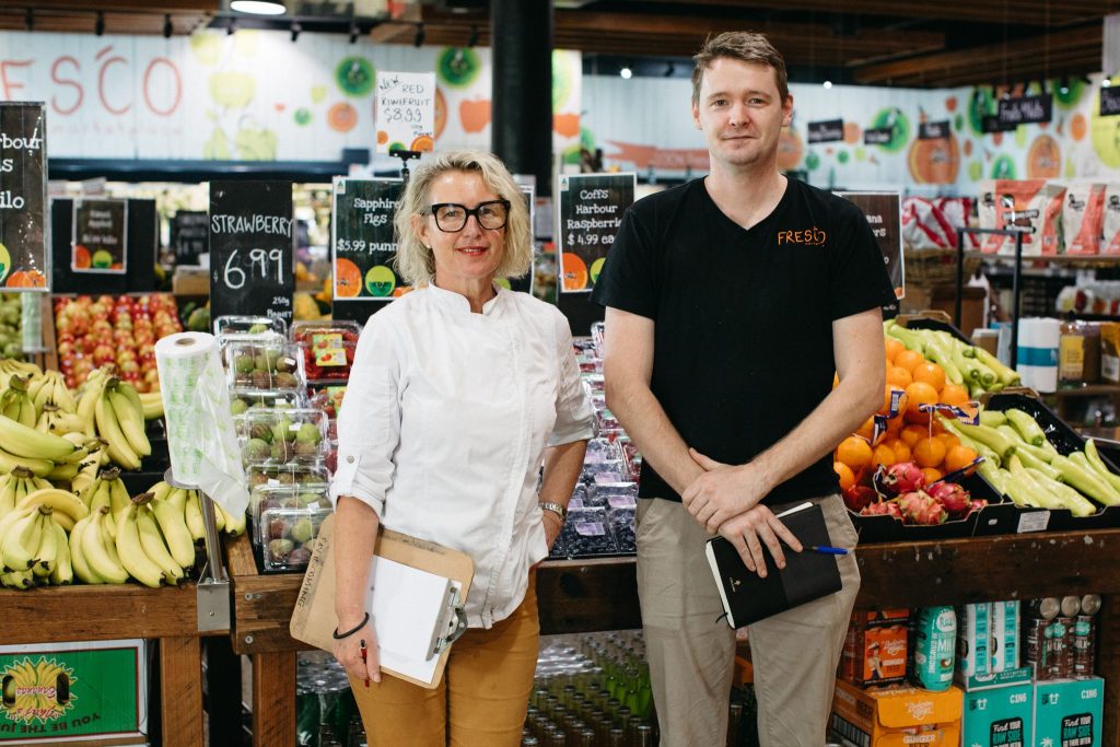 A man and a woman standing in front of a green grocer 