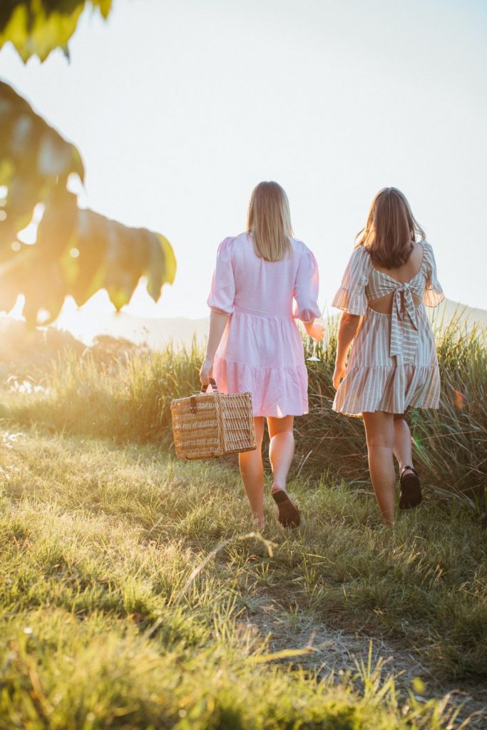 Two young women walking towards sunset holding a picnic basket