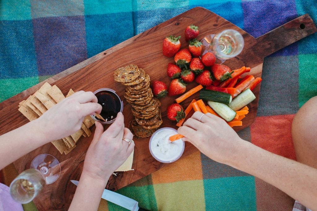 Top down shot of a wooden chopping board with strawberries, cheese, carrots and crackers on it 