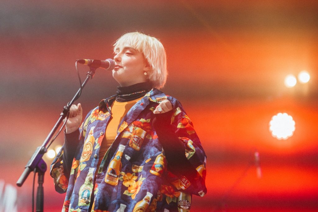 A young woman sings on stage under colourful lights 