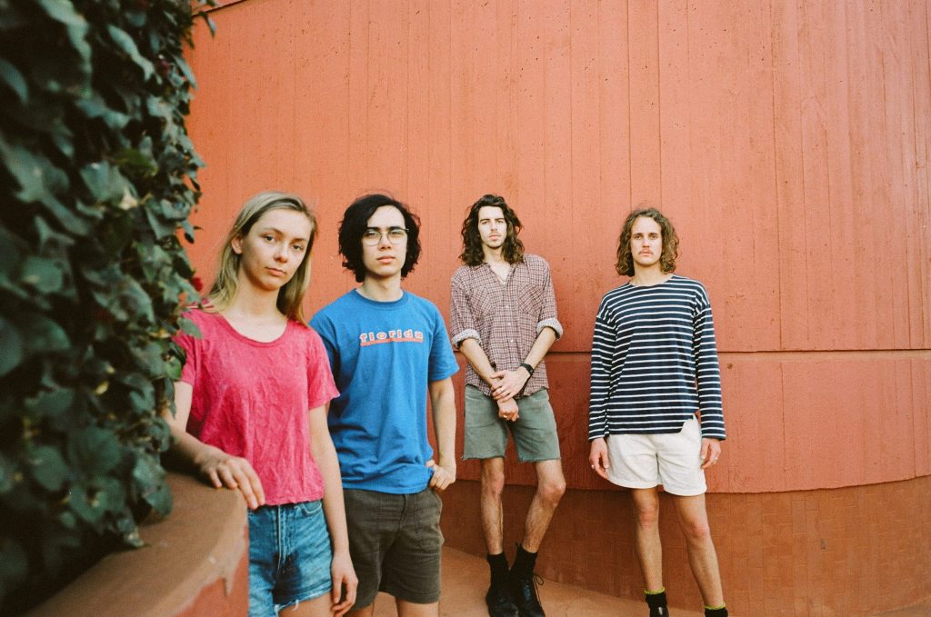 Three young men and a young woman pose against an orange backdrop