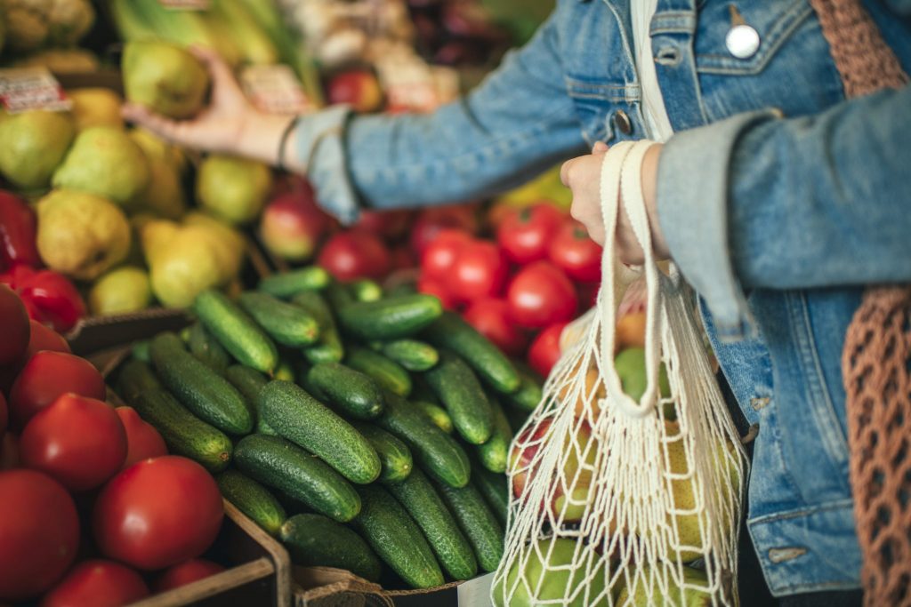 Person putting vegetables into a string bag