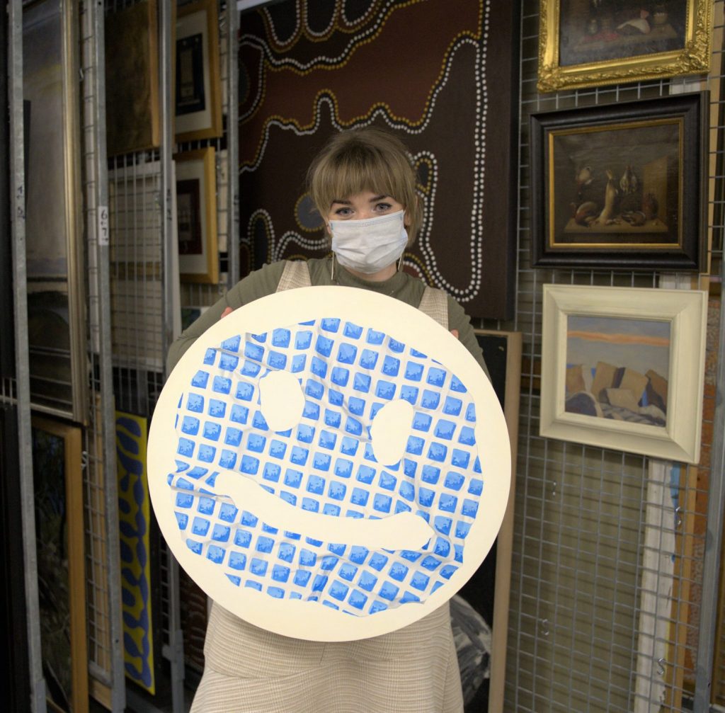 A young woman wearing a surgical mask holding an art work 