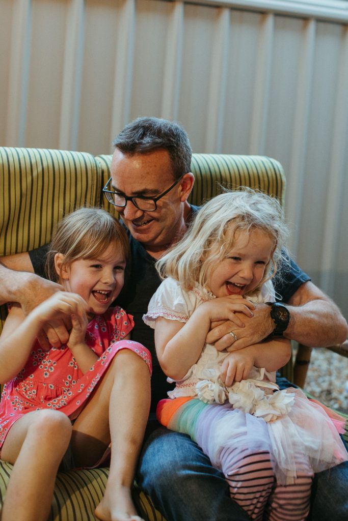 A dad cuddles his young daughters 