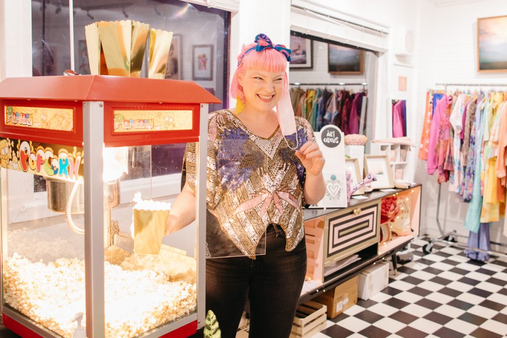 A smiling woman stands next to a popcorn machine