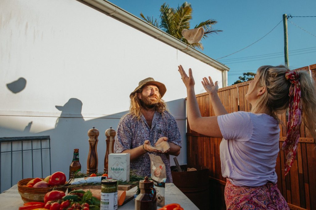 A man and woman toss pizza bases