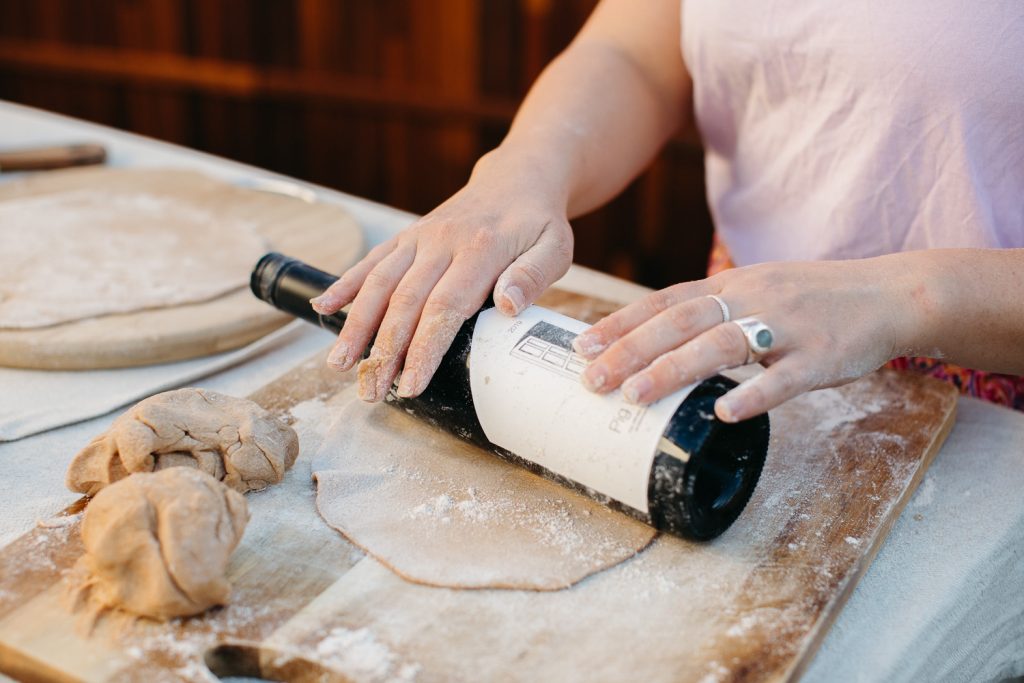 Hands rolling pizza dough with a wine bottle