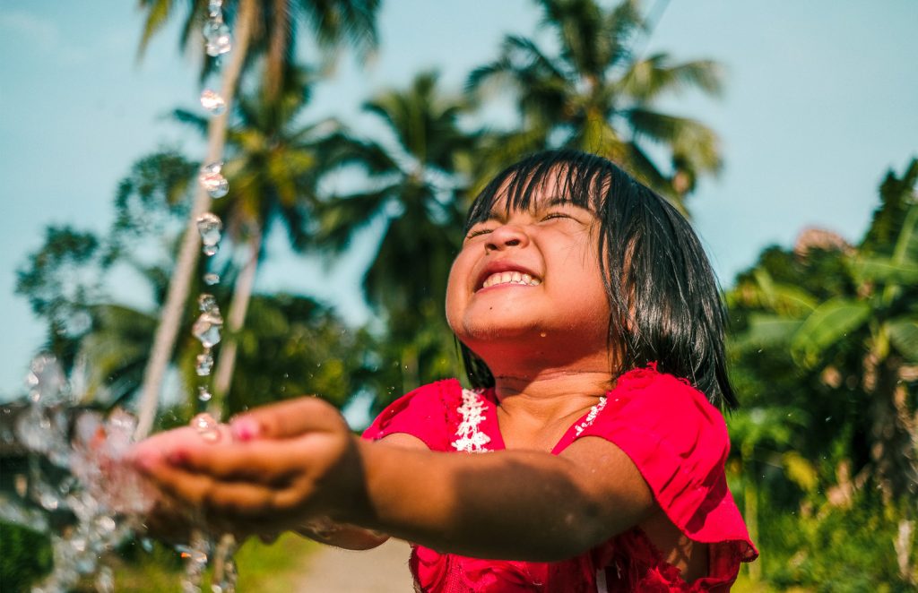 A little Indonesian girl with her hands under a tap